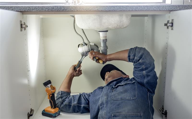 Plumber repairing pipes beneath a bathroom sink in Vancouver