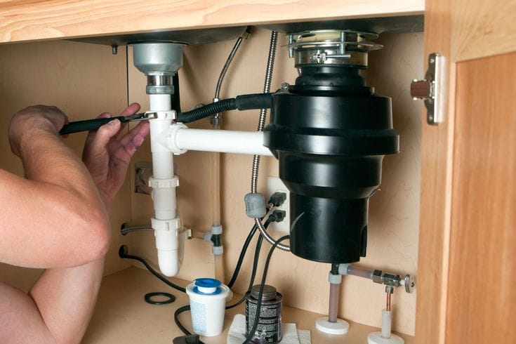 Plumber installing a garbage disposal beneath a kitchen sink in Vancouver