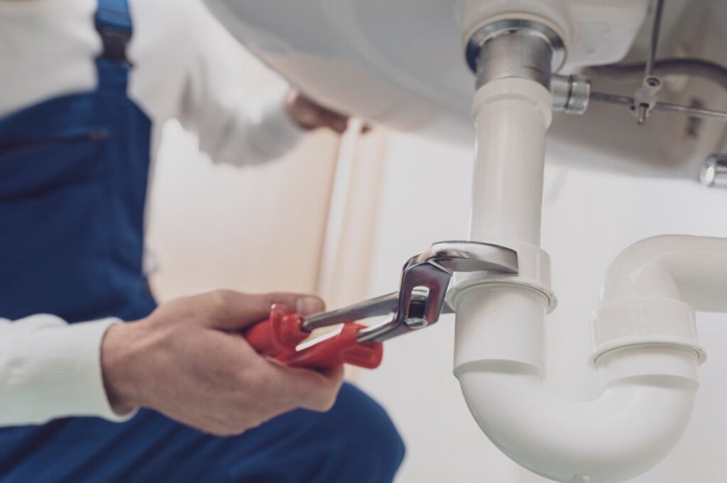Plumber repairing a white drain pipe beneath a sink in Vancouver