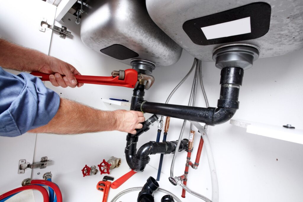 Plumber repairing drain pipes beneath a kitchen sink in Vancouver